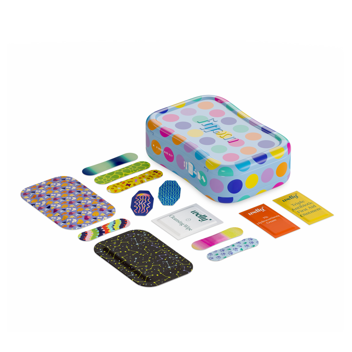 A colorful, open tin from the Welly Kids First Aid Kit showcases various adhesive bandages scattered in front. The flexible fabric bandages feature vibrant patterns and colors, with some strip-shaped and others wider. Two small packages marked medy+ are also visible.