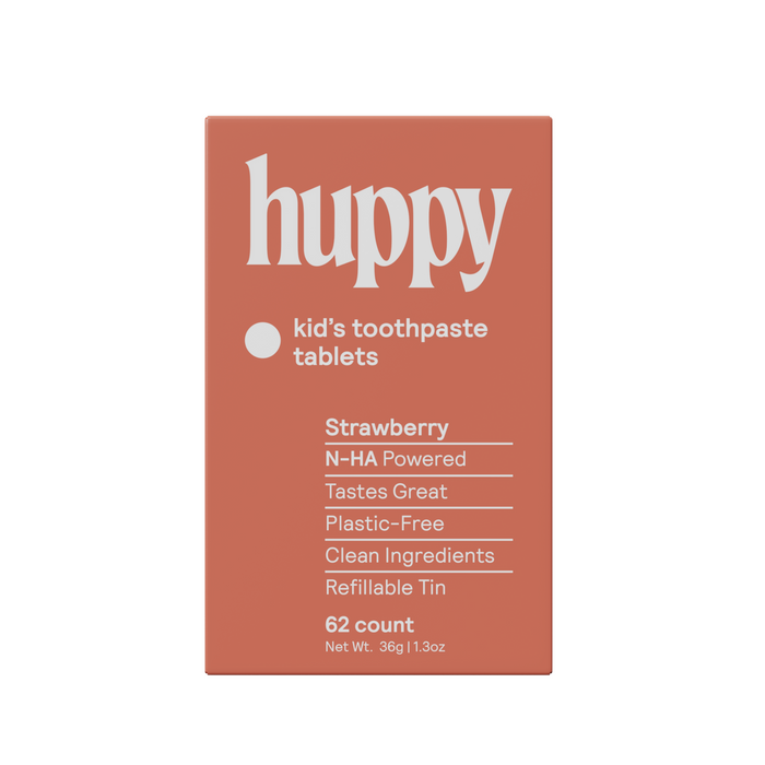 A rectangular orange box labeled Huppy Kids n-HA Toothpaste Tablets with Tin, featuring strawberry flavor, cavity-fighting nano-hydroxyapatite, clean ingredients, a plastic-free refillable tin, and 62 tasty tablets.