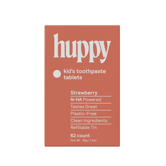 A rectangular orange box labeled Huppy Kids n-HA Toothpaste Tablets with Tin, featuring strawberry flavor, cavity-fighting nano-hydroxyapatite, clean ingredients, a plastic-free refillable tin, and 62 tasty tablets.