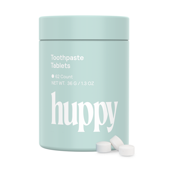 A light blue Huppy Kids n-HA Toothpaste Tablets with Tin (62 count) is shown, along with three nano-hydroxyapatite toothpaste tablets placed beside the container.