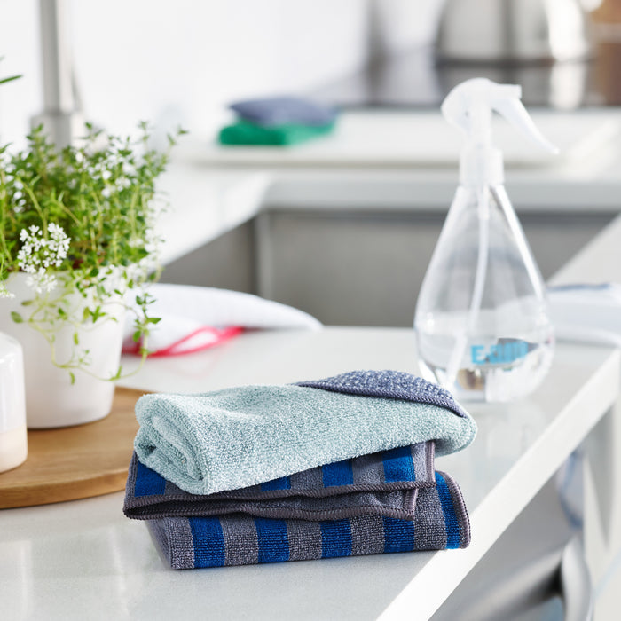 On a kitchen counter, an E-Cloth Kitchen Pack sits beside a clear spray bottle for chemical-free cleaning, while a green plant in a white pot complements the background with softly blurred kitchen items.