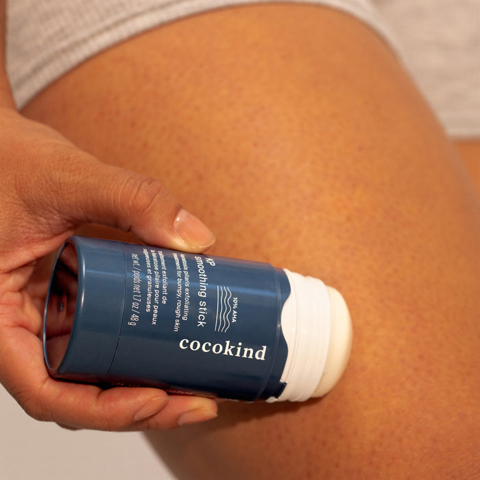 A person applies Cocokinds KP Smoothing Stick to their thigh for Keratosis Pilaris treatment, highlighting the hand and skin benefiting from its AHA exfoliants.