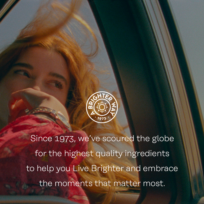 A woman with long hair gazes out of a car window with the wind blowing her hair. The text reads: "Since 1973, we’ve scoured the globe for the highest quality ingredients to help you Live Brighter and embrace the moments that matter most." Logo: "Brighter Way 1973".