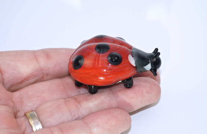 Close up of red glass ladybug cremains keepsake being held on a fingertip