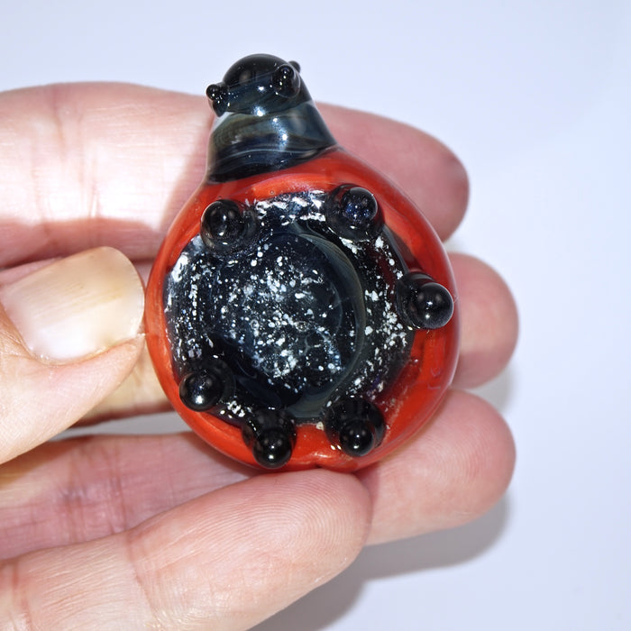 Close-up of red glass ladybug cremains pendant held between fingers