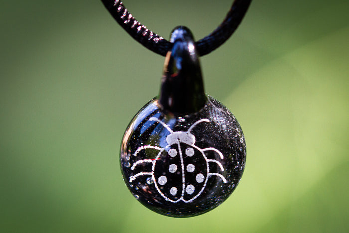 Dark glass pendant with a white holographic ladybug design infused with cremation ash on an adjustable cord.
