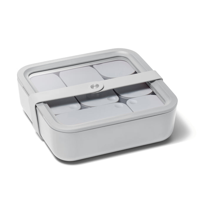 The Caraway Large Glass Food Container is a square, light gray lunch box with a transparent lid and white elastic strap. Its non-toxic, showcases an organized interior through the clear surface, and its minimalist modern design combines style with practicality.