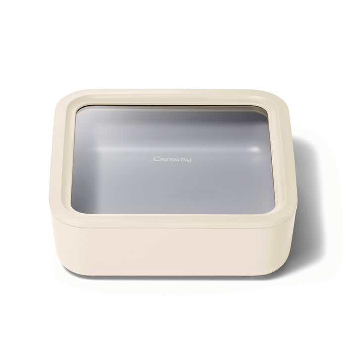 The Caraway Large Glass Food Container, featuring a beige square shape with a translucent gray lid, offers non-toxic, ceramic-coated glass storage to safely keep your essentials on a white background.