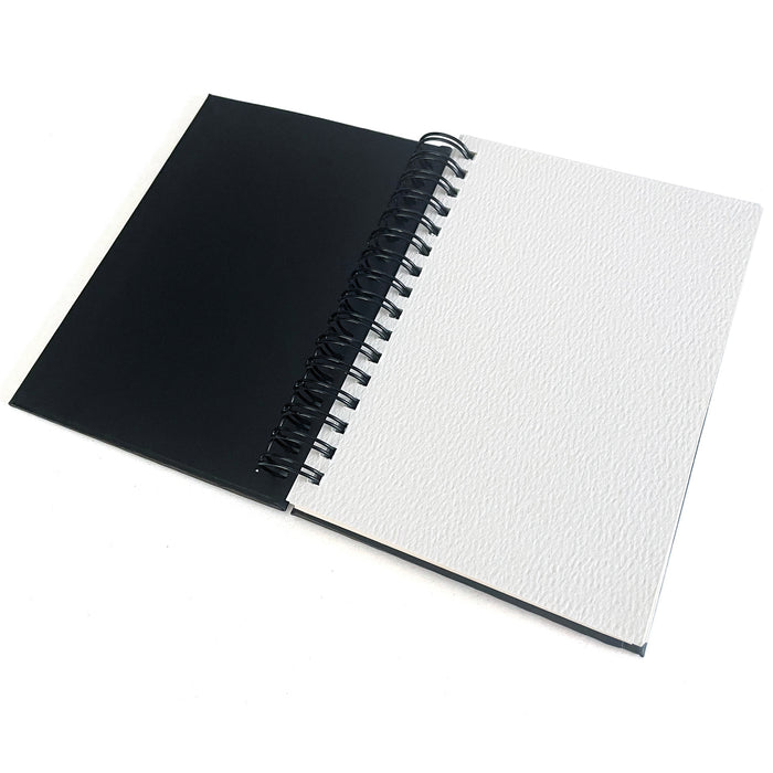 The Elseware Unplug Large Watercolor Paper Pad is pictured open, spiral-bound with a black cover and a blank, textured cold press page, displayed on a white background.