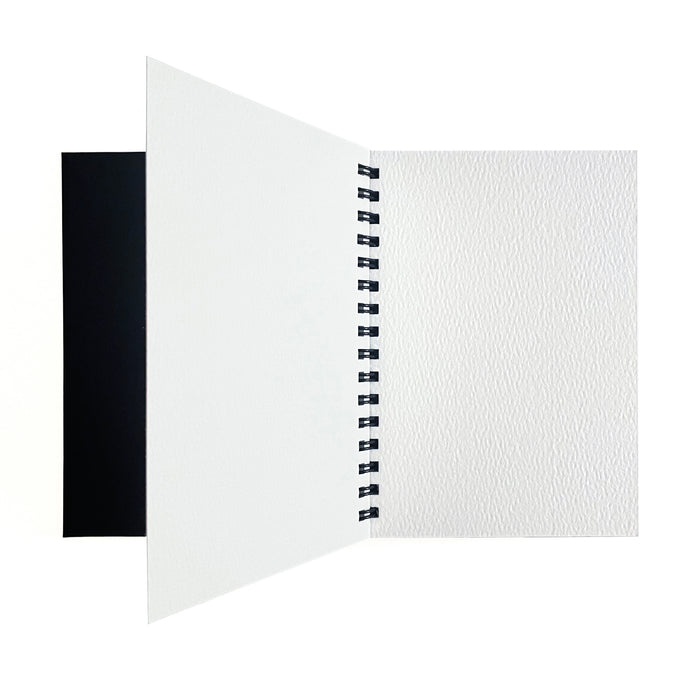The Elseware Unplug Large Watercolor Paper Pad is shown open on a white background, revealing a blank textured cold press page and a partially turned left page over a black cover.