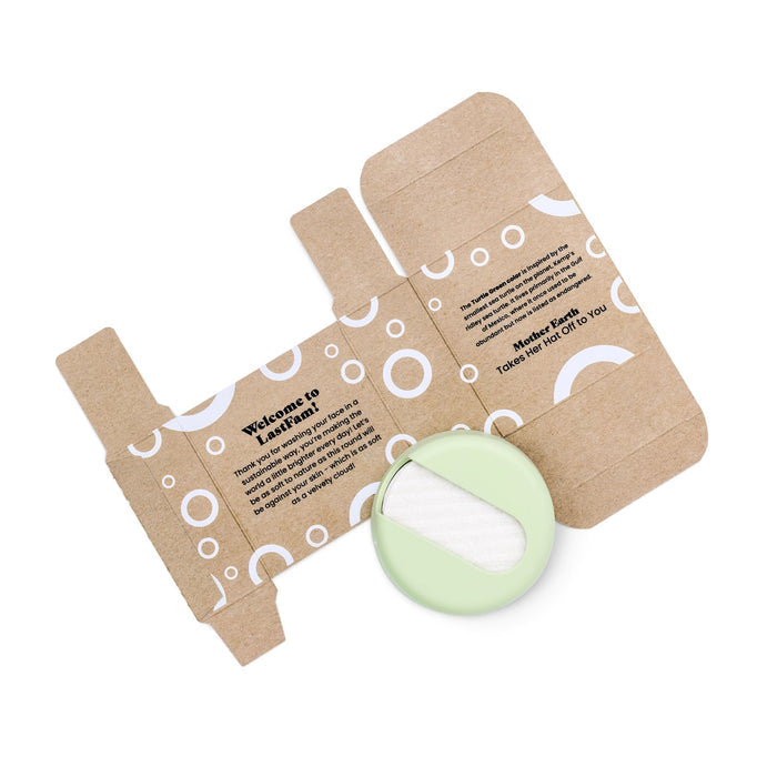 The packaging features white circular graphics and text on cardboard. The product, LastRound by LastObject, is a light green compact with a white applicator sponge. Inside it reads, “Mother Earth Takes Her Hat Off to You, showcasing sustainable beauty through its eco-friendly design.