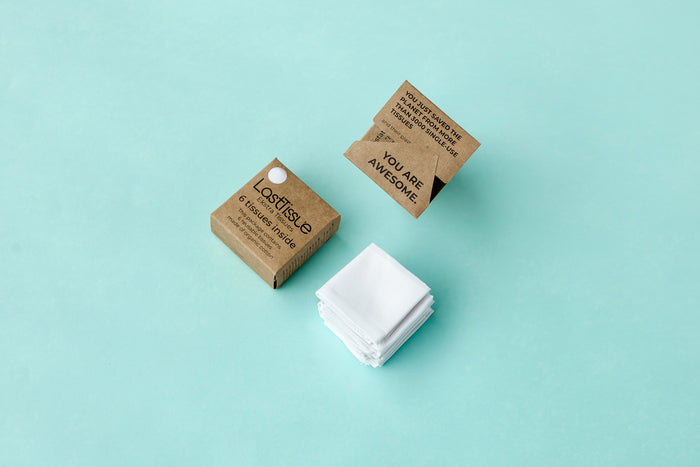 LastTissue Refill by LastObject features reusable tissues in a box made from recycled ocean-bound plastic. An open box showcases tissues with a YOU ARE AWESOME message. Organic cotton tissues are stacked beside the boxes, all against a light blue background.