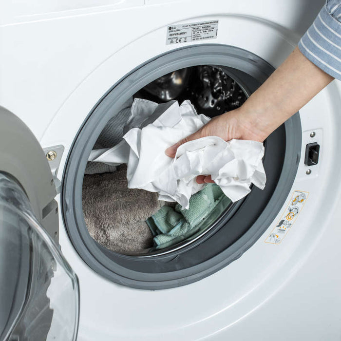 A person in a striped sleeve loads white clothes into an efficient front-loading washer. This pristine machine represents eco-friendly dedication, similar to LastObjects commitment to sustainability with their LastTissue Refill, made from recycled ocean-bound plastic for everyday use.