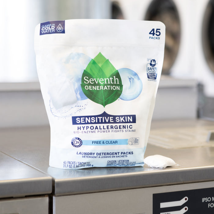 A package of Seventh Generation Laundry Detergent Packs - Sensitive Skin sits on a washing machine. The white packaging with a green leaf logo emphasizes its plant-based, fragrance-free formula. A single pod is placed beside it, ideal for sensitive skin.