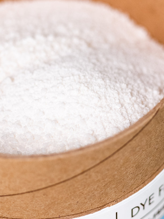 A close-up shows Melioras Laundry Powder, a round cardboard container filled with white granules. Its coarse texture emphasizes its eco-friendly nature, while a label declares it synthetic fragrance-free.