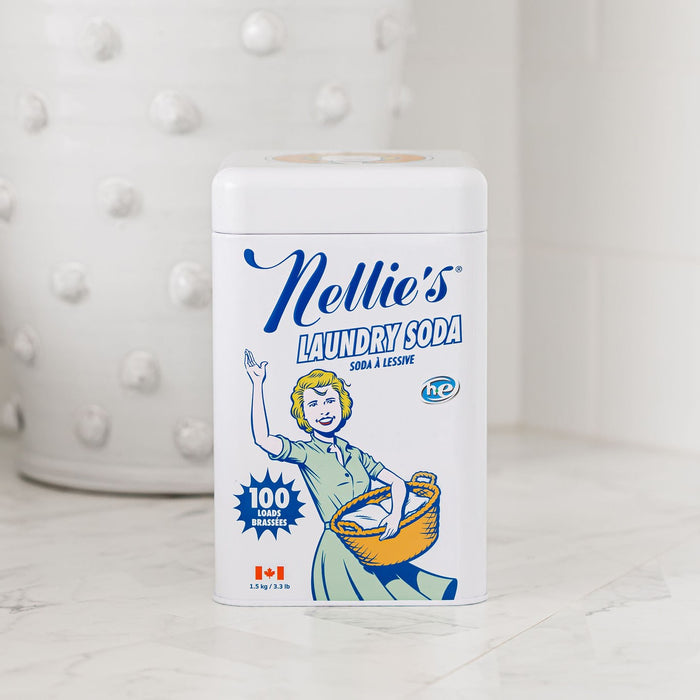 A white rectangular tin of Nellies Laundry Soda, featuring a vintage-style illustration and 100 Loads with a Canadian flag symbol, sits against a white tiled wall.