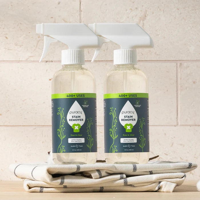 Two bottles of Laundry Stain Remover on a folded cloth, set against a light brick background.