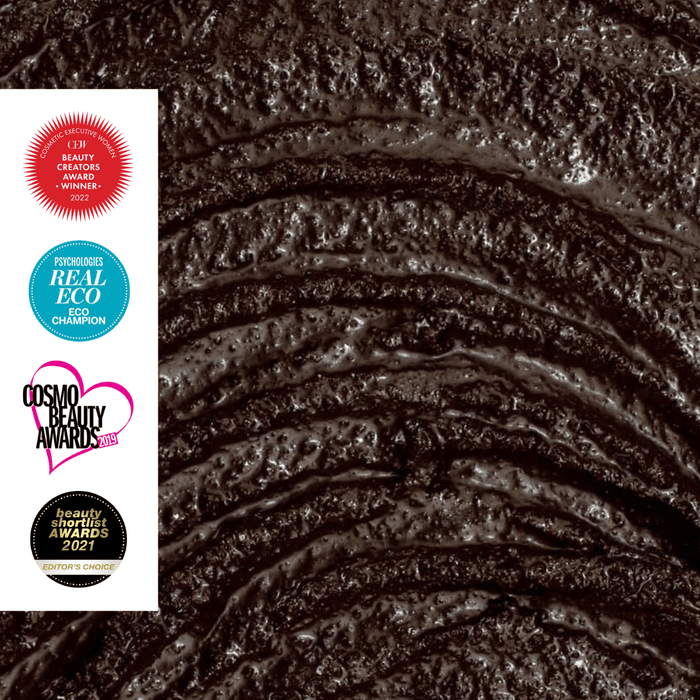 Close-up of a textured, dark brown substance with a glossy appearance. To the left, there are four circular award badges: "ELLE Beauty Creators Award 2022," "Real Eco Eco Champion," "Cosmo Beauty Awards 2023," and "Beauty Health Awards 2023 Editor's Choice.