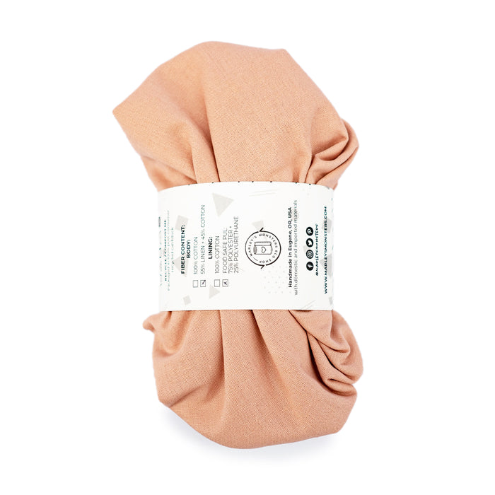 The Linen Bowl Cover Bundle - Rose by Marleys Monsters features eco-friendly, reusable solutions. Wrapped in a white paper label, the peach-colored fabric includes care instructions and branding, presenting a soft and neatly packaged product.