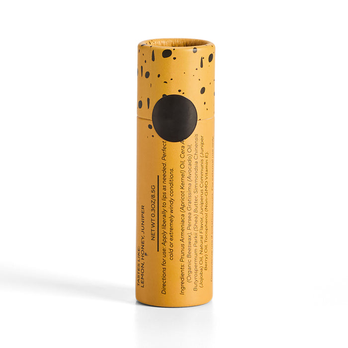 Soap Distillery Lip Balm comes in a yellow cylindrical cardboard tube with black speckles, a black top circle, and vertically printed text listing organic beeswax and natural ingredients.
