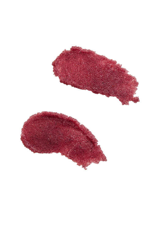 Two shimmery raspberry-colored smears of Henné Organics Lip Exfoliator adorn a white background, showcasing a creamy, slightly metallic texture with sugar crystals for exfoliation.