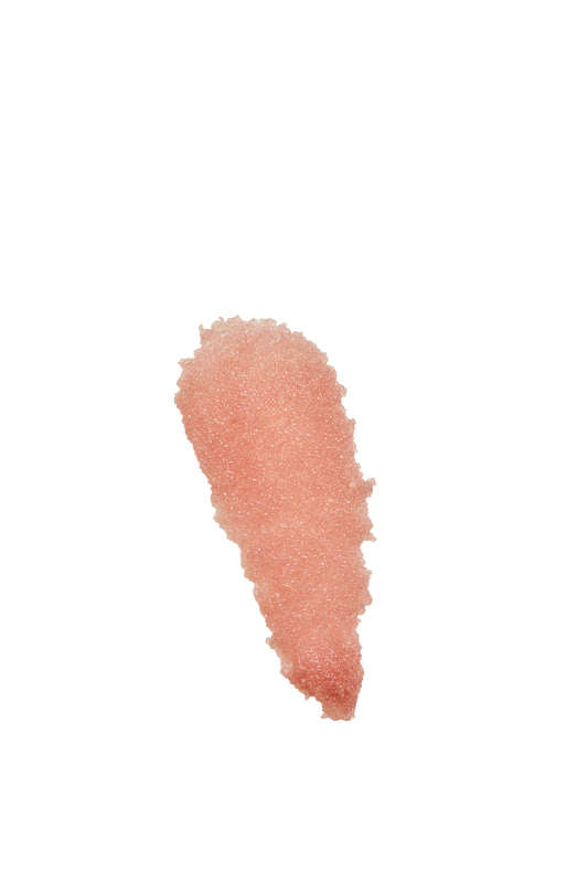 A smooth smear of peach-pink Lip Exfoliator by Henné Organics on a white background reveals a gritty texture similar to sugar crystals, indicating the use of organic ingredients for gentle yet effective exfoliation.