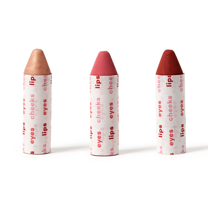Three Axiology Lip-to-Lid Balmies, labeled eyes, lips, and cheeks, stand upright on a white background. The vibrant Cotton Candy Skies set features light brown, pink, and red tips, offering a zero waste beauty option without excess packaging.
