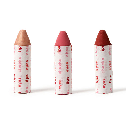 Three Axiology Lip-to-Lid Balmies, labeled eyes, lips, and cheeks, stand upright on a white background. The vibrant Cotton Candy Skies set features light brown, pink, and red tips, offering a zero waste beauty option without excess packaging.