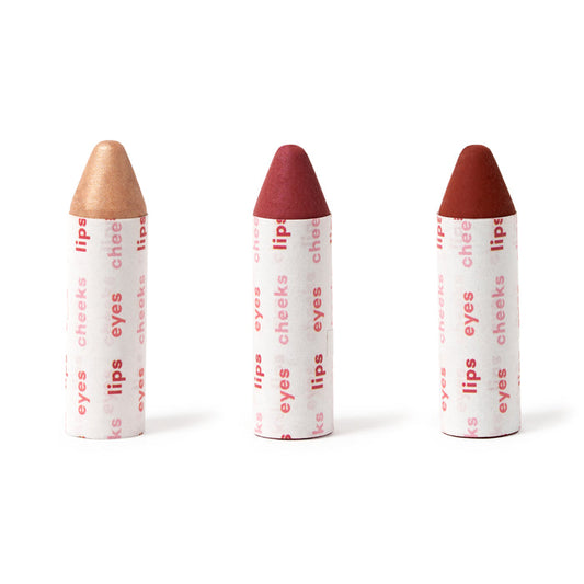 Axiologys Lip-to-Lid Balmies Set - Of the Earth, featuring vegan sticks in bronze, pink, and red shades for lips, eyes, and cheeks, is aligned vertically on a white background. The packaging promotes zero waste makeup with natural beauty emphasis.