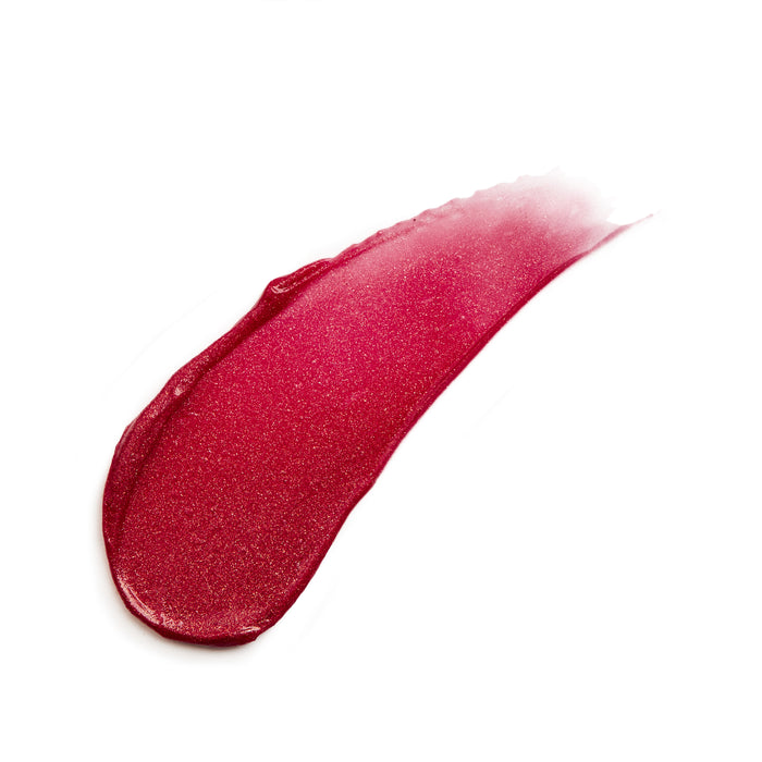 A red lipstick smear on a white background, demonstrating a glossy texture with a hint of shimmer. The thick swipe tapers smoothly to a thin end, reminiscent of the luxurious feel of Kari Grans Lip Whip Color Balm.