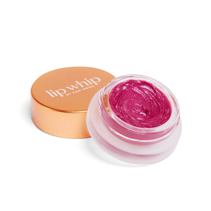A small glass jar of shimmering pink Lip Whip Color Balm by Kari Gran with an open gold lid sits on a white background. Made with natural ingredients, it has a creamy texture and is elegantly labeled Lip Whip by Kari Gran on the lid.