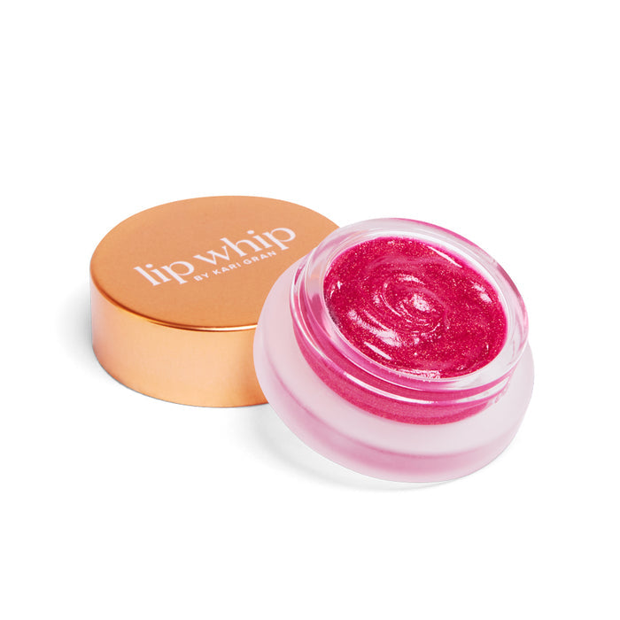 An open jar of Kari Gran Lip Whip Color Balm with a shimmery pink hue sits beside its closed golden lid, elegantly inscribed with Lip Whip. Made from natural ingredients, the stylish container rests against a pristine white background.