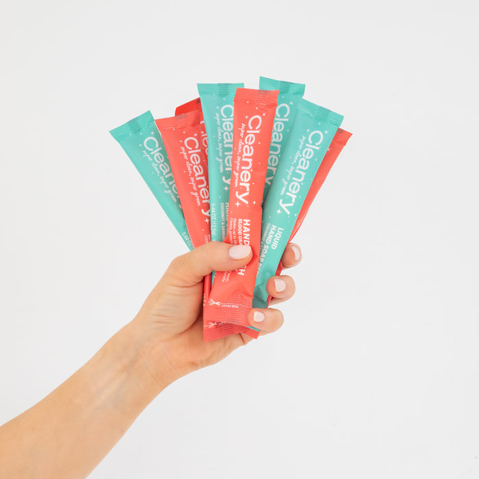 A hand displays five vibrant stick packets of Cleanerys Liquid Hand Soap Starter Kit against a white background. The teal and coral packets highlight Mango and Mojito scents, ideal for sensitive skin, making these convenient refills essential.