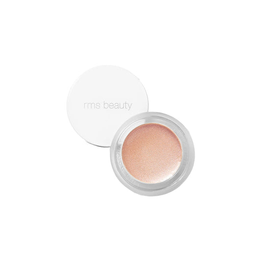 A small round pot of RMS Beauty’s Champagne Rosé Luminizer with a white lid, shown open to reveal a shimmery, champagne-toned cream highlighter for a natural dewy glow. The lid features “rms beauty” in light grey text.