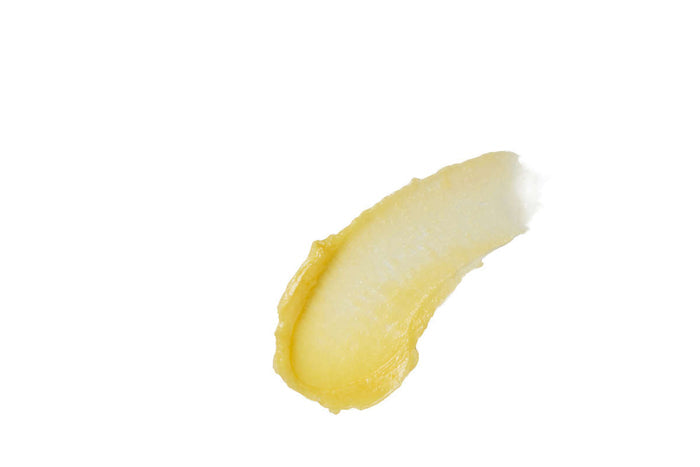 A smooth, glossy smear of Henné Organics Luxury Lip Balm, in creamy light yellow, sits on a plain white background, reminiscent of an organic treat for lips.