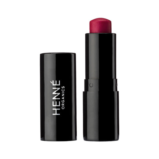 A black lipstick tube labeled Henne Organics Luxury Lip Tint stands next to its matching cap, displaying a rich, deep red hydrating lip color against a white background.