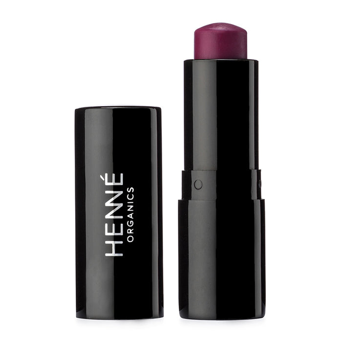 A dark purple Luxury Lip Tint, cap off, sits beside a black lid labeled Henné Organics, in a sleek black cylindrical tube on a white background.