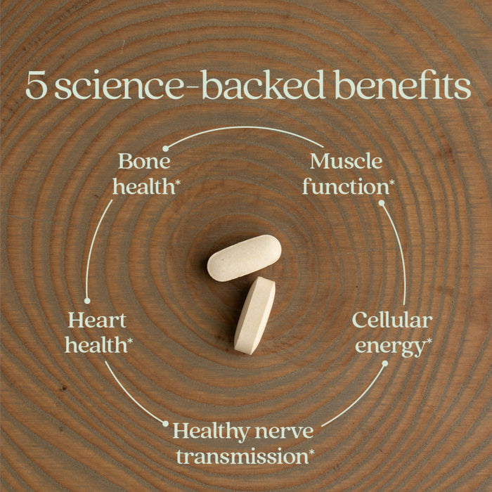 Two white tablets on a wooden surface with text: "5 science-backed benefits" in a circular layout. Benefits include bone health, muscle function, heart health, cellular energy, and healthy nerve transmission.