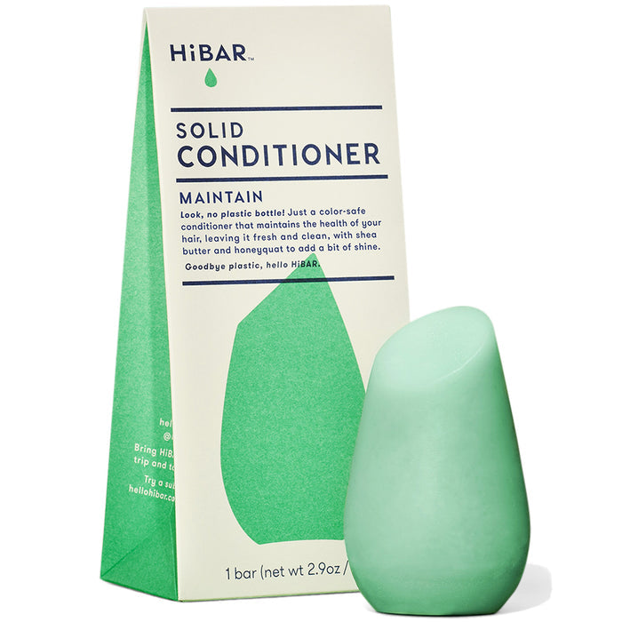 A green, teardrop-shaped HiBAR Maintain Solid Conditioner bar sits in front of its box, which is light green and blue. The packaging emphasizes eco-friendliness and highlights the benefits for dry hair with its natural ingredients.