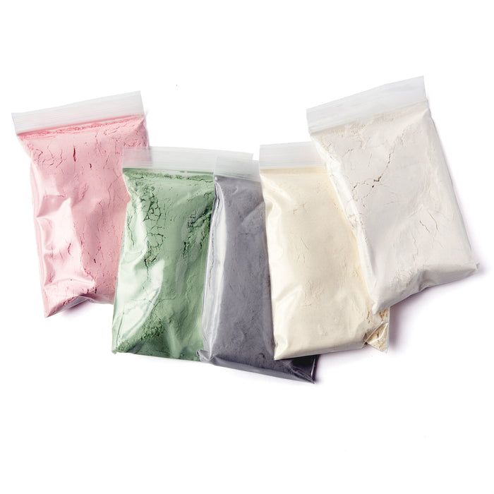The Make Your Own Eco-Dough Set by eco-kids includes five plastic bags with food-grade powder in pink, green, gray, black, and white. Ideal for tactile exploration, these ingredients are neatly lined up against a white background.