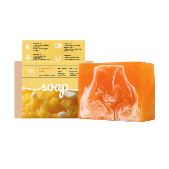 A rectangular orange and white handcrafted Soapymania Mango Coconut Sorbet Hydrating Bar Soap sits in front of its yellow and beige packaging featuring product info and mango images. Made with natural vegan ingredients.