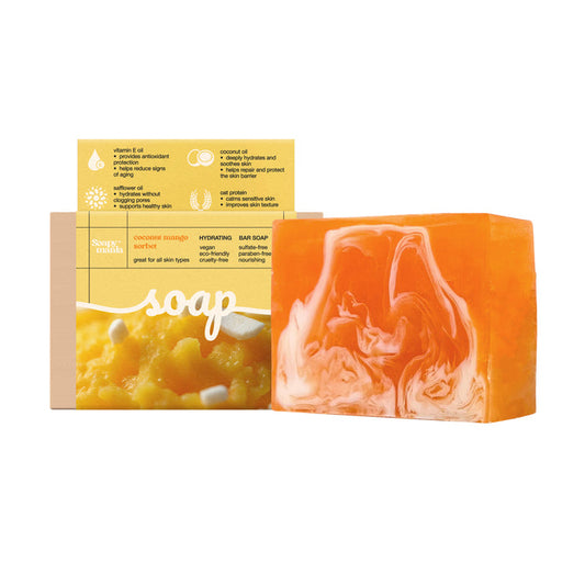 A rectangular orange and white handcrafted Soapymania Mango Coconut Sorbet Hydrating Bar Soap sits in front of its yellow and beige packaging featuring product info and mango images. Made with natural vegan ingredients.