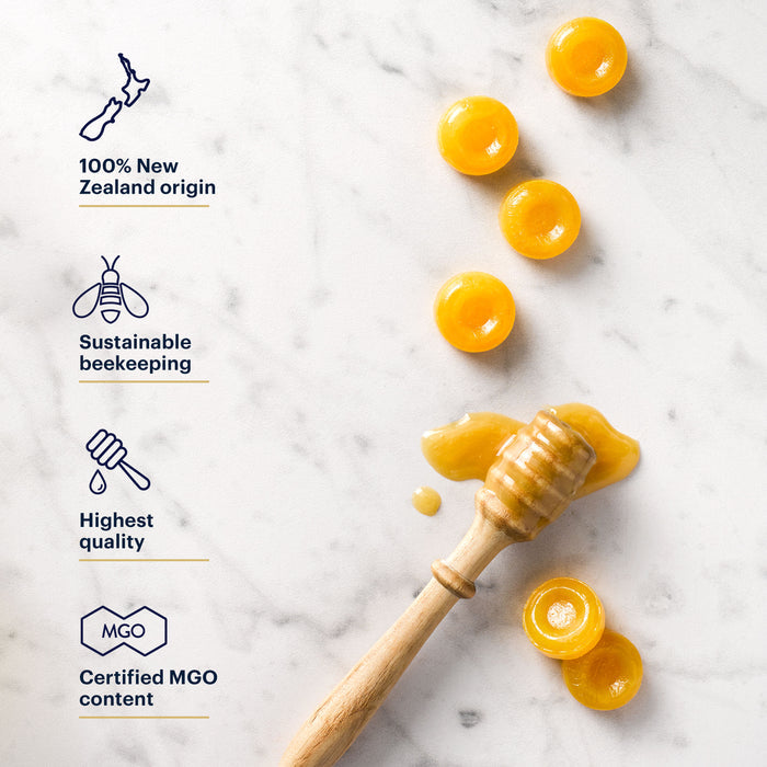 Honey lozenges on a marble surface with a honey dipper. Text highlights 100% New Zealand origin, sustainable beekeeping, highest quality, and certified MGO content.
