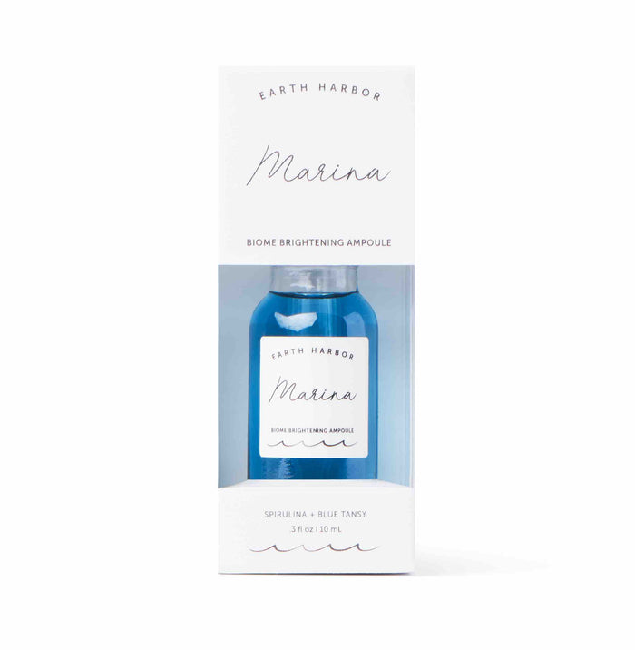 A clear box displays the Earth Harbor MARINA Biome Brightening Ampoule, a blue glass bottle labeled with white and blue text. The minimalist design highlights ocean-blue botanicals like spirulina and blue tansy, nurturing your skin microbiome with this brightening ampoule serum.