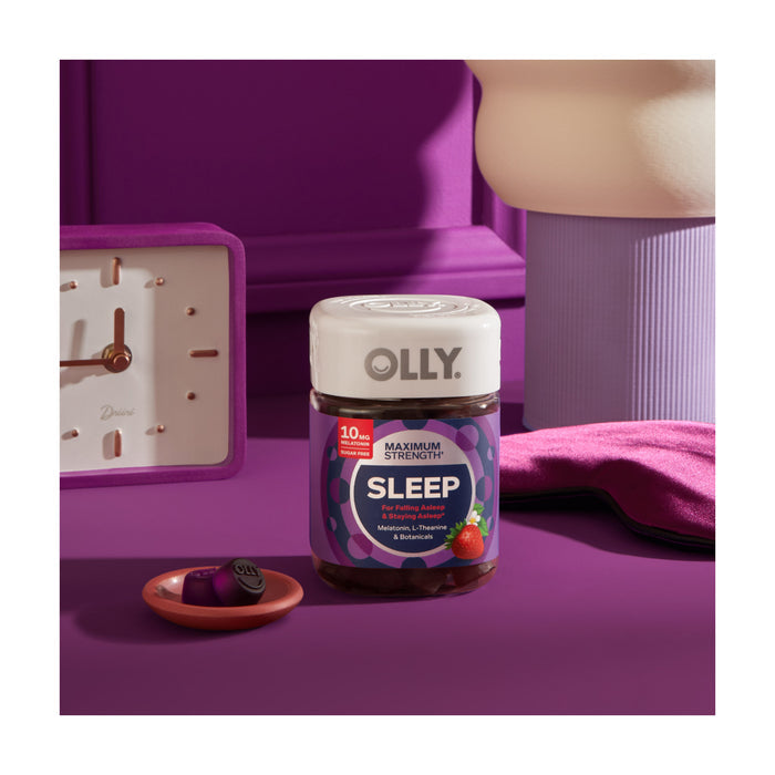 A jar of OLLY Maximum Strength Sleep Gummies with melatonin sits on a purple surface surrounded by a clock, lamp, and sleep mask in calming purple hues. An open dish of vibrant gummies awaits to help you drift into restful slumber.