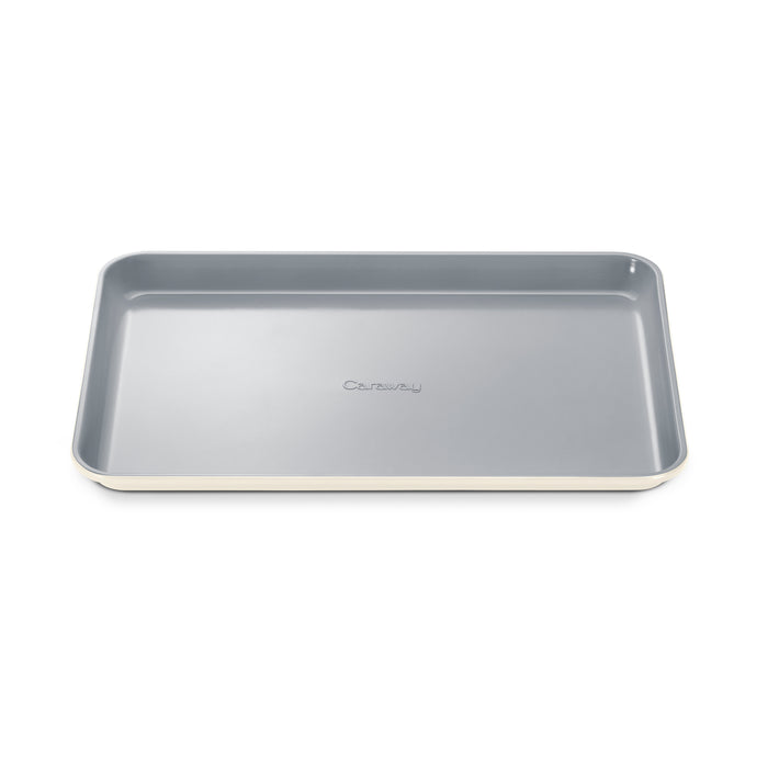 The Medium Ceramic Baking Sheet from Caraway features a non-stick gray inner surface and elegant white outer rim. It has raised edges, an embossed brand name, and a non-toxic ceramic coating for healthy baking.