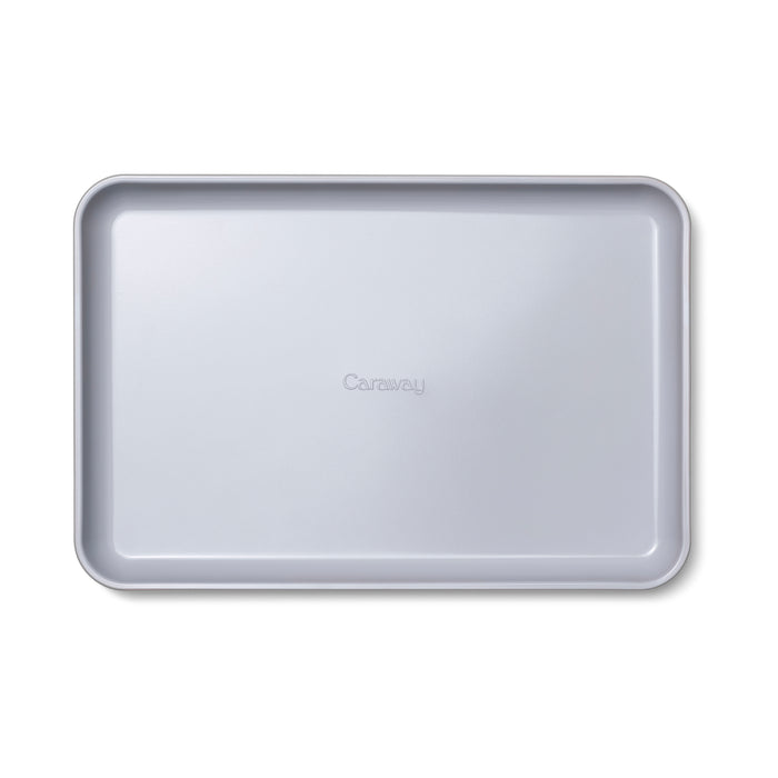 The Medium Ceramic Baking Sheet by Caraway is a rectangular, light gray baking sheet with slightly raised edges. It features Caraway embossed at the center and a smooth, non-stick ceramic-coated surface, making it perfect for healthy baking.