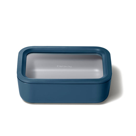 A rectangular dark teal airtight ceramic-coated glass food container with a transparent lid sits on a white background. The lid prominently displays Caraway, highlighting its non-toxic design and innovative Air Release technology. Known as the Medium Glass Food Container, it exemplifies practical elegance.