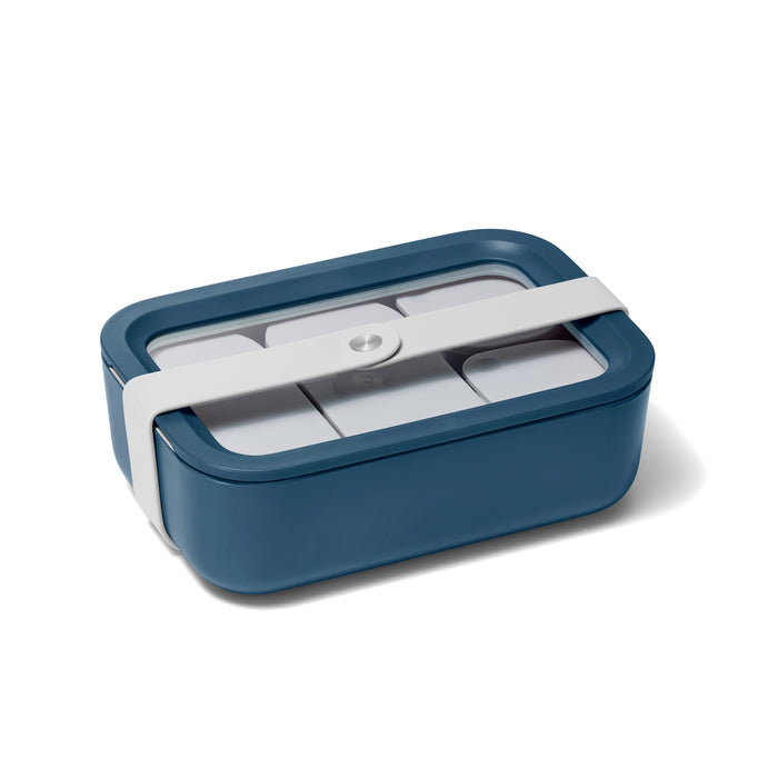 The Caraway Medium Glass Food Container is a rectangular, dark teal lunchbox with rounded edges and a transparent ceramic-coated glass lid, secured by a wide white elastic band. It features an elegant, minimalist design and is likely crafted from durable, non-toxic plastic.