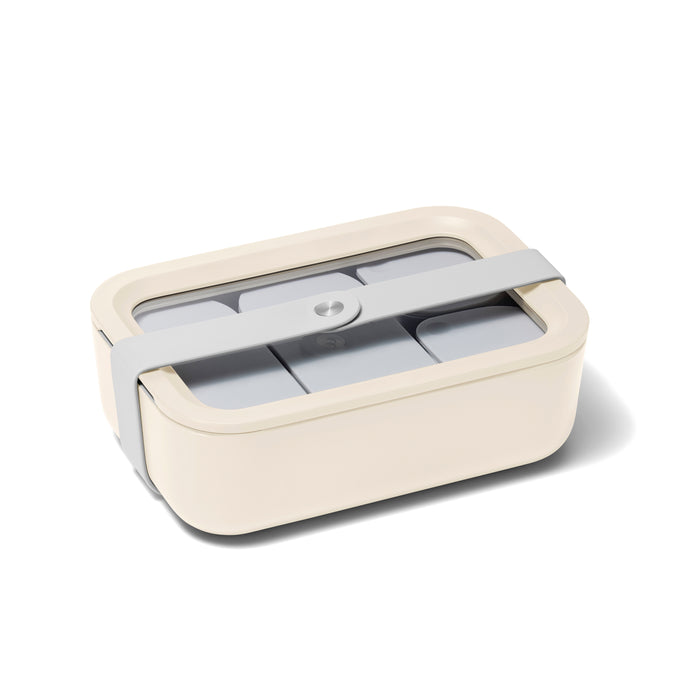 A beige rectangular Caraway Medium Glass Food Container features a gray lid with Air Release technology and a central circular button. Made from non-toxic materials, it includes a matching gray strap and is isolated on a white background.
